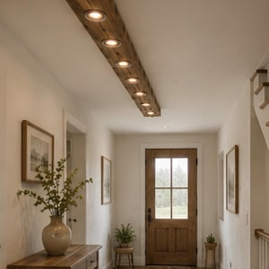 May include: A rectangular ceiling light fixture made from a long, dark brown wooden beam. The beam features six evenly spaced, circular recessed spotlights that emit a warm, focused light downward into the hallway space below.