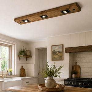 May include: A rectangular ceiling light fixture made of natural wood with a visible grain pattern. The fixture features three evenly spaced, square black recessed spotlights integrated into the wood, providing downward illumination.