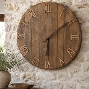 May include: A large circular wall clock constructed from vertical brown wooden planks. The clock face features raised, dark brown Roman numerals and two thin, dark brown metal hands positioned to indicate the time near seven o'clock.
