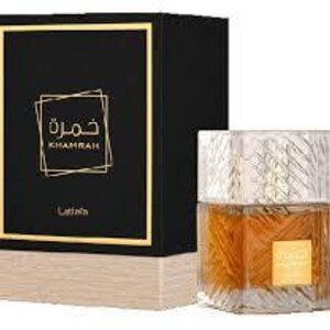 May include: A perfume bottle and its box. The bottle is clear with a gold-coloured liquid inside. The box is black with gold trim and the Arabic word "Khamrah" in gold. The box has a light brown base.