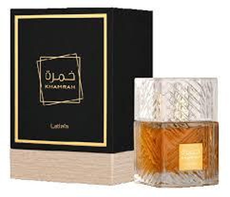 May include: A perfume bottle and its box. The bottle is clear with a gold-coloured liquid inside. The box is black with gold trim and the Arabic word "Khamrah" in gold. The box has a light brown base.