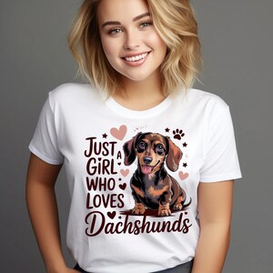 May include: White t-shirt with a graphic of a dachshund dog and the text "Just a Girl Who Loves Dachshunds". The design includes hearts, paw prints, and stars. The dog is brown and black.