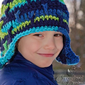 May include: A young boy wearing a blue and green crocheted hat with ear flaps. The hat has a blue and green striped pattern. The boy is smiling and looking at the camera.