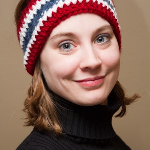 May include: A woman wearing a red, white, and blue crocheted headband. She is wearing a black turtleneck sweater.