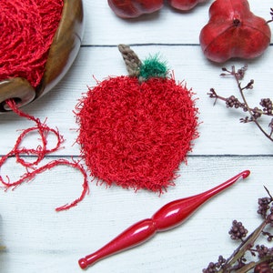 May include: A red crocheted apple with a green stem and leaf, yarn, a crochet hook, and a wooden yarn bowl.