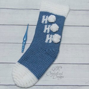 May include: A blue and white crocheted Christmas stocking with the word "HO HO HO" in white yarn and white pom-poms.