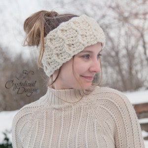 Puede incluir: Una diadema de crochet de color crema con un patrón de punto de cable. La diadema la lleva puesta una persona con el pelo castaño recogido en una coleta.