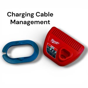 May include: A red Milwaukee M12 battery charger and a blue oval-shaped plastic ring. The text Charging Cable Management is displayed above the items. The charger features a vented top surface and a label with battery status icons.