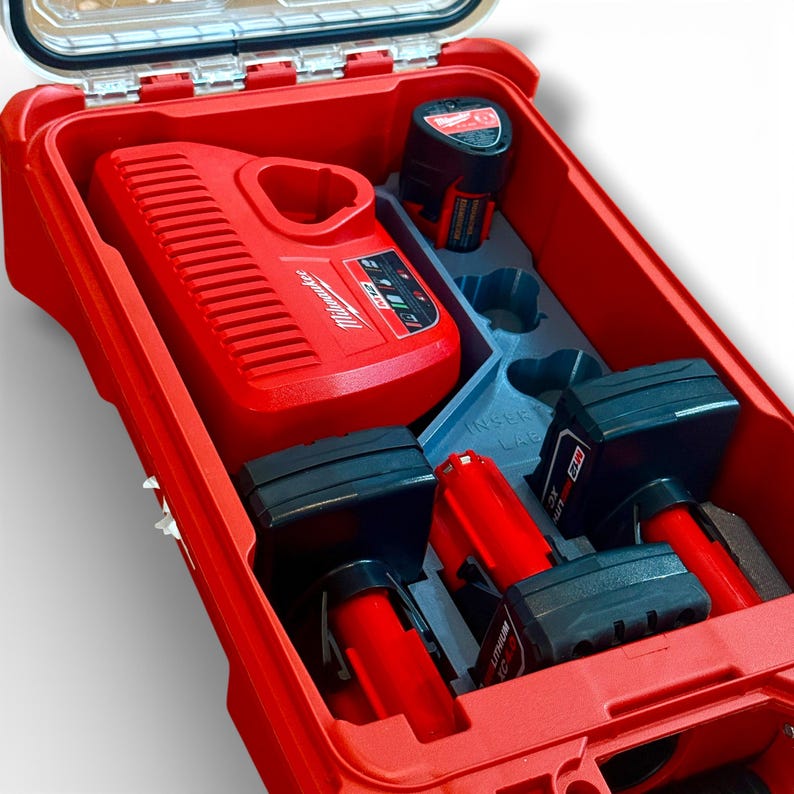 May include: Red tool case with a clear lid, open to reveal a red charger and several black and red battery packs. The charger is labeled "Milwaukee". The case has a gray insert to hold the batteries.