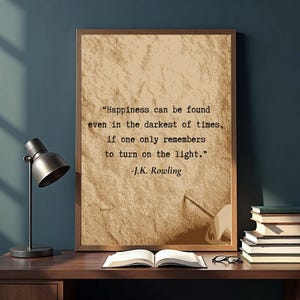 May include: A framed print with a quote by J.K. Rowling on a textured background. The quote reads, "Happiness can be found even in the darkest of times, if one only remembers to turn on the light." A desk lamp, books, and glasses are also visible.