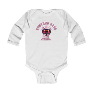Puede incluir: Body de bebé blanco de manga larga con un gráfico de un gato con gafas de esquí y el texto "STEVENS PASS CASCADES WASHINGTON" en rosa. El body está hecho de material suave.