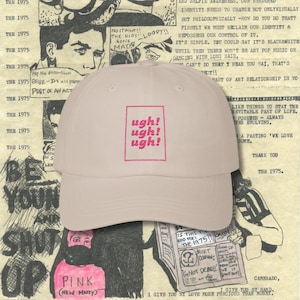 Puede incluir: Gorra de béisbol rosa claro con el texto "ugh! ugh! ugh!" en un cuadrado rosa. La gorra tiene un diseño clásico de seis paneles, una visera curva y una correa ajustable.
