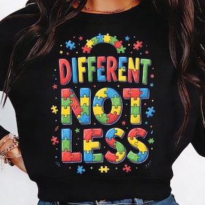 Könnte beinhalten: Schwarzes Sweatshirt mit dem Schriftzug "DIFFERENT NOT LESS" in bunten Puzzleteil-Buchstaben. Das Design beinhaltet einen Regenbogen und Sterne. Das Sweatshirt ist ein Rundhals-Stil.