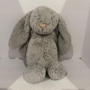 May include: A plush, gray bunny rabbit with long, floppy ears and a soft, textured appearance. The bunny has a light brown nose and is designed to be a cuddly toy. The toy is made of a soft, fuzzy material.