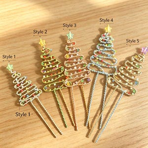 May include: Five wire hair pins shaped like Christmas trees, labeled Style 1 through Style 5. Each pin features a twisted wire frame decorated with small colorful beads and topped with a small star. The pins vary in wire color and bead placement.