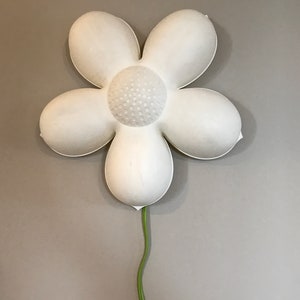 May include: A white flower-shaped wall light with a textured centre and a green cord.