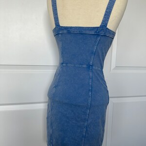 May include: A light blue denim dress with a square neckline and thin straps. The dress has a fitted silhouette and a short length.
