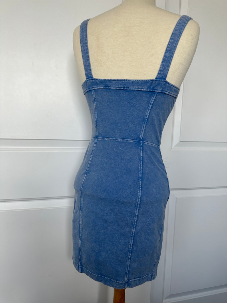 May include: A light blue denim dress with a square neckline and thin straps. The dress has a fitted silhouette and a short length.