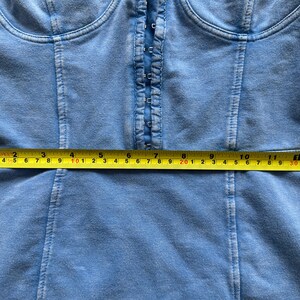 May include: A blue denim corset top with a front zipper closure. The top is measured with a tape measure, showing a measurement of 30 inches.
