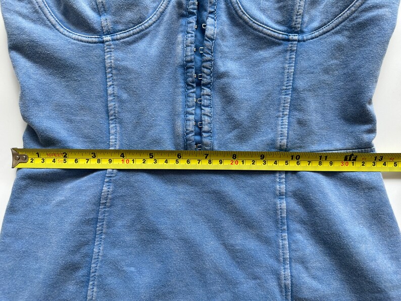 May include: A blue denim corset top with a front zipper closure. The top is measured with a tape measure, showing a measurement of 30 inches.