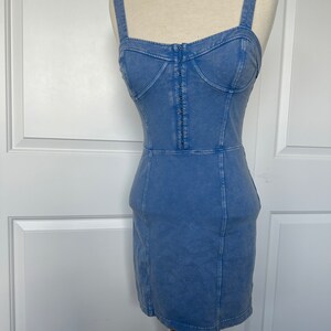 May include: A light blue denim dress with a fitted bodice and a straight skirt. The dress has a zipper closure in the front and adjustable straps.