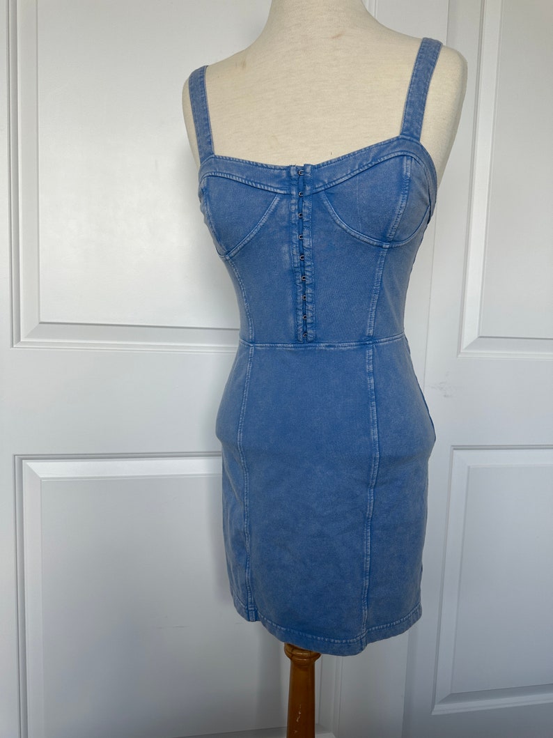 May include: A light blue denim dress with a fitted bodice and a straight skirt. The dress has a zipper closure in the front and adjustable straps.