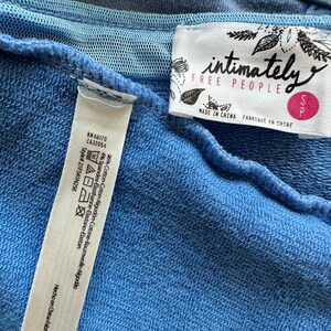 May include: A blue cotton sweatshirt with a white tag that says "intimately free people" and "Made in China" in black text. The tag also has a small pink tag that says "S".