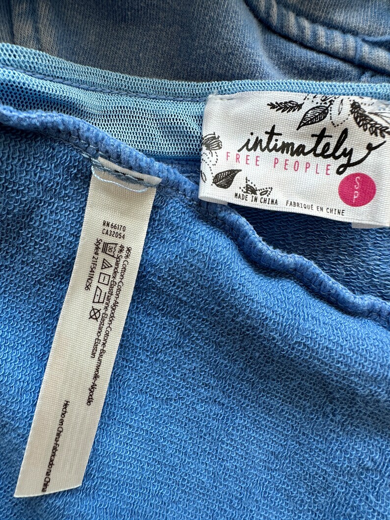 May include: A blue cotton sweatshirt with a white tag that says "intimately free people" and "Made in China" in black text. The tag also has a small pink tag that says "S".
