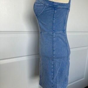 May include: A light blue denim dress with a fitted silhouette and thin straps. The dress has a slightly faded look and is made of a soft, comfortable fabric.