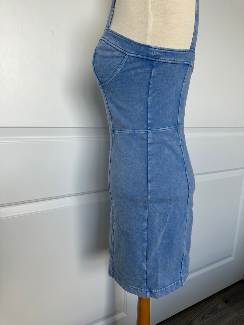 May include: A light blue denim dress with a fitted silhouette and thin straps. The dress has a slightly faded look and is made of a soft, comfortable fabric.