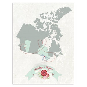 May include: A map of Canada with a red dotted line connecting two red heart pins. The line forms a heart shape. The text "Ashley + Ryan" is written in red with the date "July 25, 2023" below it. The map is on a white background with a light gray texture.