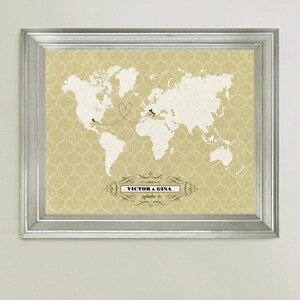 May include: A framed world map print with a heart-shaped line connecting two locations. The map is on a beige background with a decorative pattern. The text "VICTOR & GINA" and "September 20" is printed below the map.