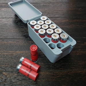May include: A grey plastic ammunition box with an open lid, containing red and silver shotgun shells. Two extra shells are visible. The shells are red with silver tops and the text "UNIVERSAL 7 1/2".