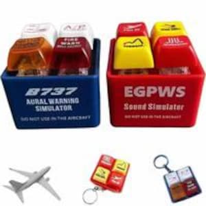 May include: Two plastic boxes, one blue and one red, each containing four colored, rectangular objects. The blue box reads "8737 AURAL WARNING SIMULATOR" and the red box reads "EGPWS Sound Simulator". A small airplane model, a keychain with four colored objects, and a keychain with four colored objects are also shown.