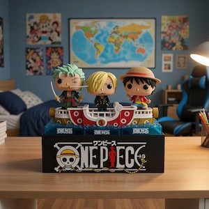 Può includere: Un set di statuette di One Piece con tre personaggi su una base a forma di nave. La base è nera con il logo di One Piece. Le statuette sono Zoro, Sanji e Luffy. Lo sfondo comprende una camera da letto con poster e una mappa del mondo.