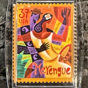 May include: Clear acrylic keychain featuring a colorful illustration of a couple dancing the Merengue. The design includes the text "37 USA" and "Merengue" with the year "2005". The artwork depicts a man in a hat and a woman with a flower in her hair.