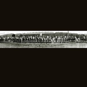 May include: A black and white panoramic photograph of a group of people on horseback, lined up in front of a train. The image is a historical photo, with text at the bottom that reads "Cow Girls of the American Round Up".