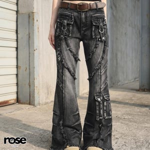 Op de afbeelding: Zwarte denim flared jeans met meerdere zakken, decoratieve stiksels en metalen hardware. De jeans hebben een distressed, vervaagde uitstraling en een bruine leren riem. Het woord "rose" staat linksonder gedrukt.