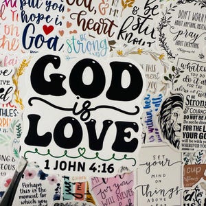 Può includere: Una collezione di adesivi con citazioni e frasi ispiratrici. L'adesivo centrale recita "Dio è Amore" in grassetto nero, con il versetto biblico 1 Giovanni 4:16 sottostante. Altri adesivi presentano disegni floreali e testo scritto a mano.