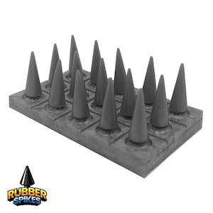 May include: A grey rubber spike mat featuring sixteen conical spikes arranged in a grid. The base is a rectangular block with square indentations. The logo "RUBBER SPIKES" is in the lower left corner.