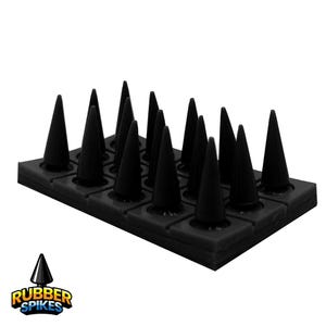 Può includere: Punte in gomma nere disposte a griglia. Le punte sono a forma di cono e si ergono da una base nera. Il nome del prodotto "RUBBER SPIKES" è visualizzato in un logo in basso.