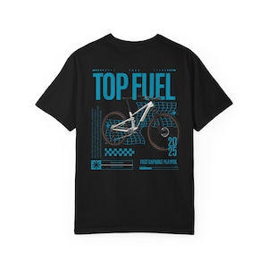 以下が含まれることがあります： 白いマウンテンバイクのイラストの上に「TOP FUEL」と書かれた、黒いTシャツ。デザインには「20 25」と「FAST CAPABLE PLAYFUL」の文字が含まれています。