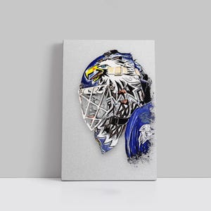 Könnte beinhalten: Leinwanddruck eines Hockey-Torwartmaske mit einem Adler-Design. Die Maske ist überwiegend weiß, blau und schwarz, mit gelben Akzenten. Der Kopf des Adlers ist prominent auf der Oberseite der Maske dargestellt.
