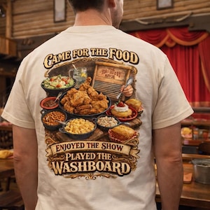 Könnte beinhalten: Cremefarbenes T-Shirt mit detaillierter Grafik, die verschiedene Gerichte wie Brathähnchen und Salate zeigt. Der Text auf dem Shirt lautet: "Game for the Food, Enjoyed the Show, Played the Washboard."