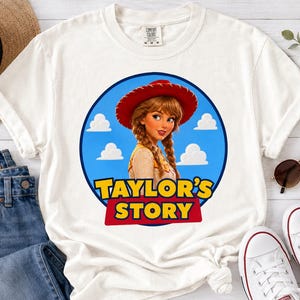 Puede incluir: Una camiseta blanca de manga corta con un gr&aacute;fico circular de un personaje de dibujos animados con trenzas y un sombrero de vaquero rojo. El fondo es azul con nubes blancas. El texto "TAYLOR'S STORY" est&aacute; impreso en letras amarillas y rojas.