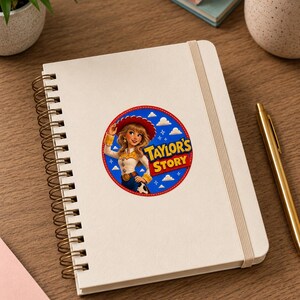 May include: A white spiral-bound notebook featuring a circular sticker on the cover. The sticker displays a cartoon cowgirl character in a red hat and yellow shirt, set against a blue sky with clouds and the text Taylor's Story in yellow letters.