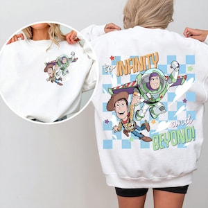 May include: White sweatshirt featuring a cartoon graphic of Woody and Buzz Lightyear in flight. The back of the sweatshirt has the text "to INFINITY and BEYOND!" in a colorful design with stars and a checkered pattern.