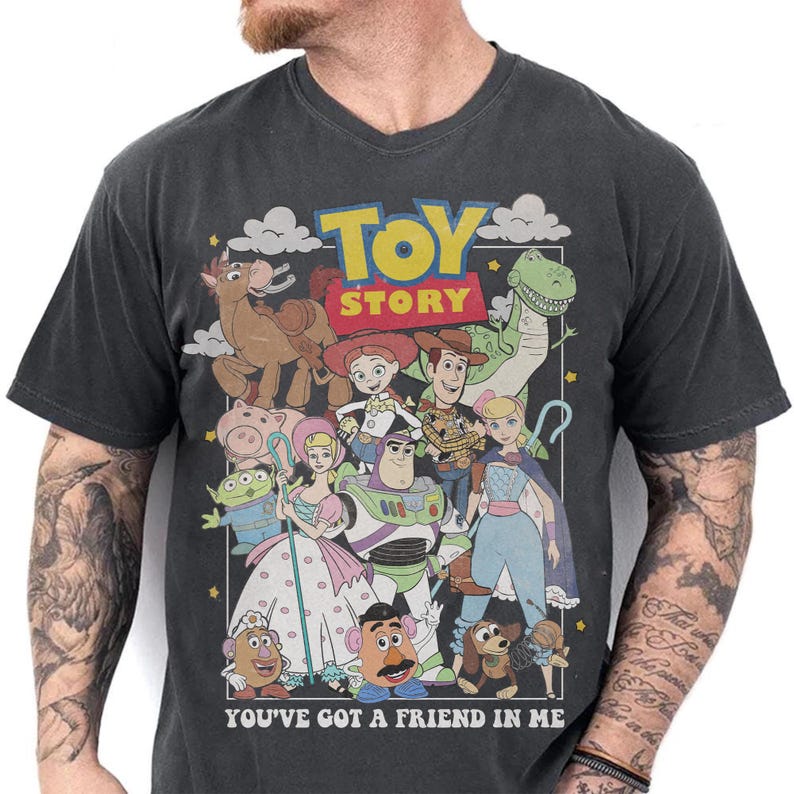 May include: Dark gray v-neck t-shirt featuring a colorful graphic of characters from the animated film "Toy Story." The design includes Woody, Buzz Lightyear, and other beloved characters, with the text "TOY STORY" and "YOU'VE GOT A FRIEND IN ME."