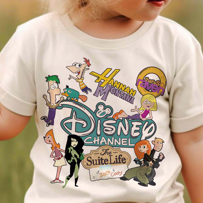 May include: Cream-coloured t-shirt featuring cartoon characters from Disney Channel shows. The shirt includes the Disney Channel logo and text for "Hannah Montana," "That's So Raven," and "The Suite Life of Zack & Cody."