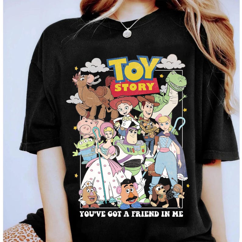 May include: Black t-shirt featuring a colorful graphic of characters from the animated film "Toy Story." The design includes Woody, Buzz Lightyear, and other beloved characters, with the words "TOY STORY" and "YOU'VE GOT A FRIEND IN ME."